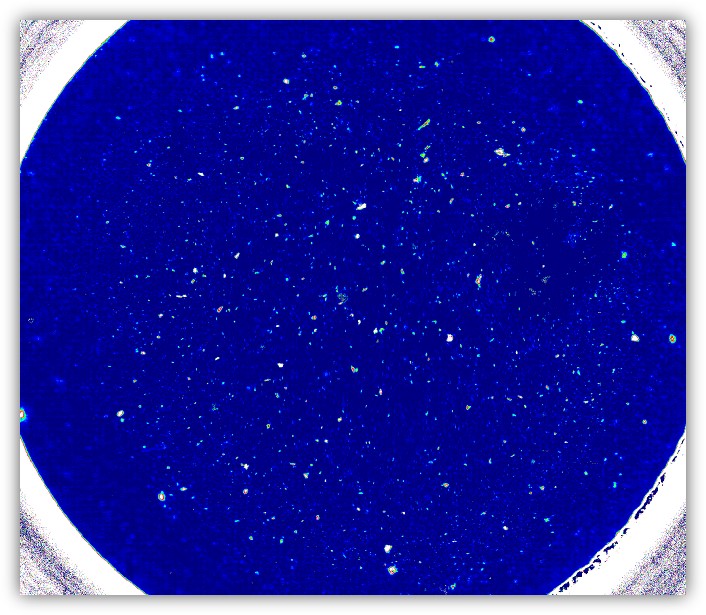IR imaging of microplastics on a filter. The particles light up as white dots on a blue background.