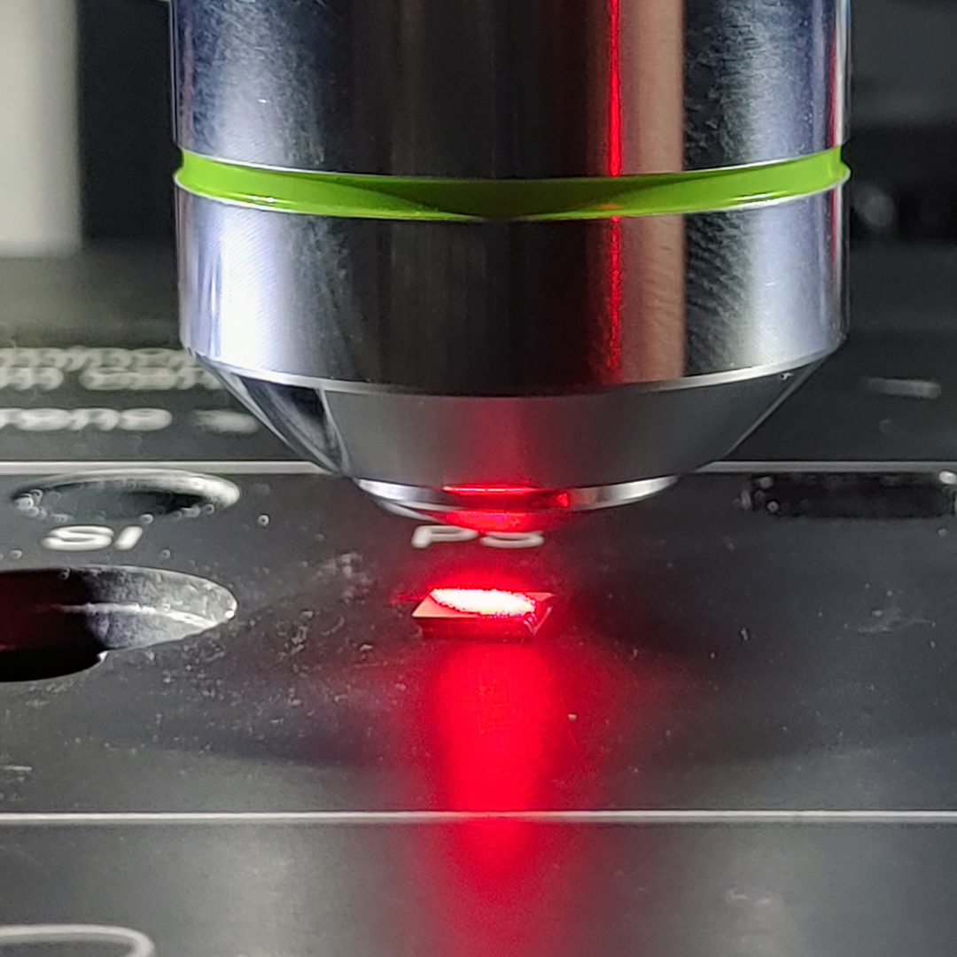 Close-up of a Raman microscope focusing a red laser on a SERS (Surface-Enhanced Raman Scattering) sample mounted on a labeled sample stage.