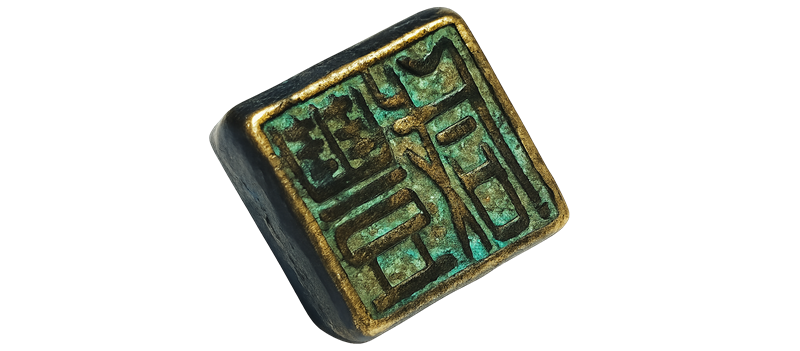 An ancient qing dynasty metal stamp. The outer rim of the stamp is yellow and shiny, the 3D characters on the stamp are dark with the inset surrounding area showing a copper-like green tinge.