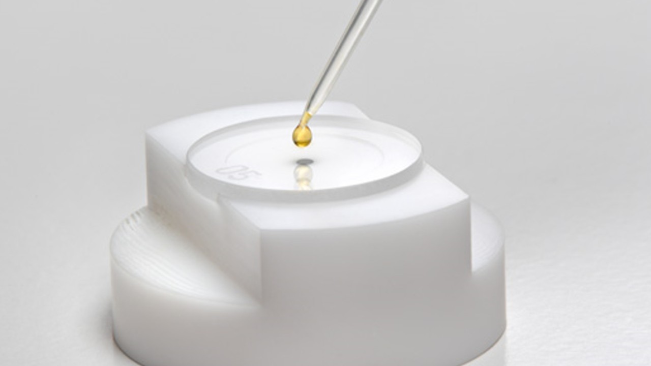 Sample holder of the S2 PICOFOX total reflection X-ray fluorescence spectrometer (TXRF) from Bruker, onto which a drop of yellow liquid is placed.