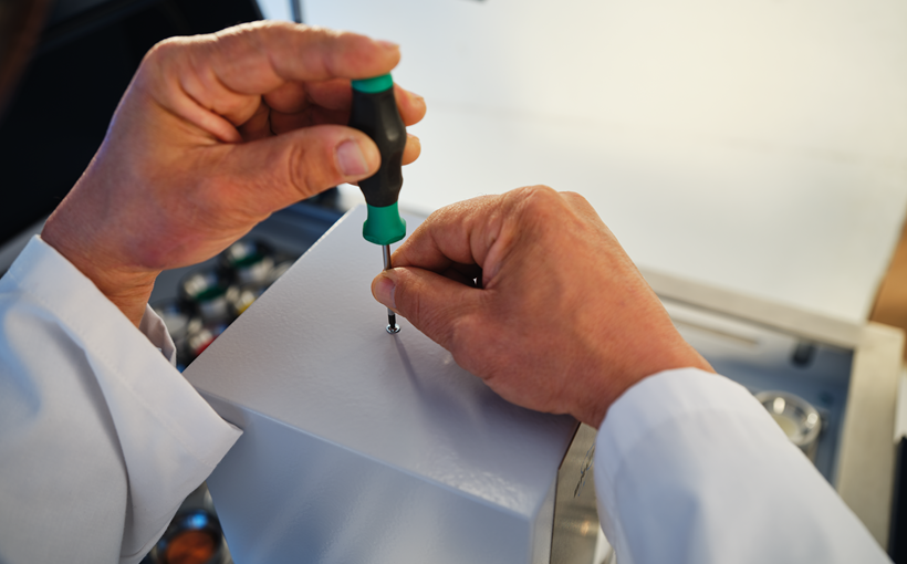 Image showing a man performing maintenance on a WDXRF spectrometer. He is screwing a component.