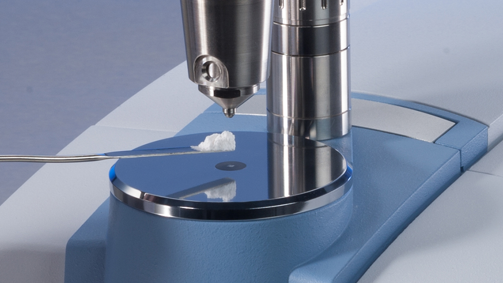 Close-up view of the sample plate of the ALPHA II FT-IR spectrometer for the analysis of white powder, which is applied to the measurement area with a spatula.