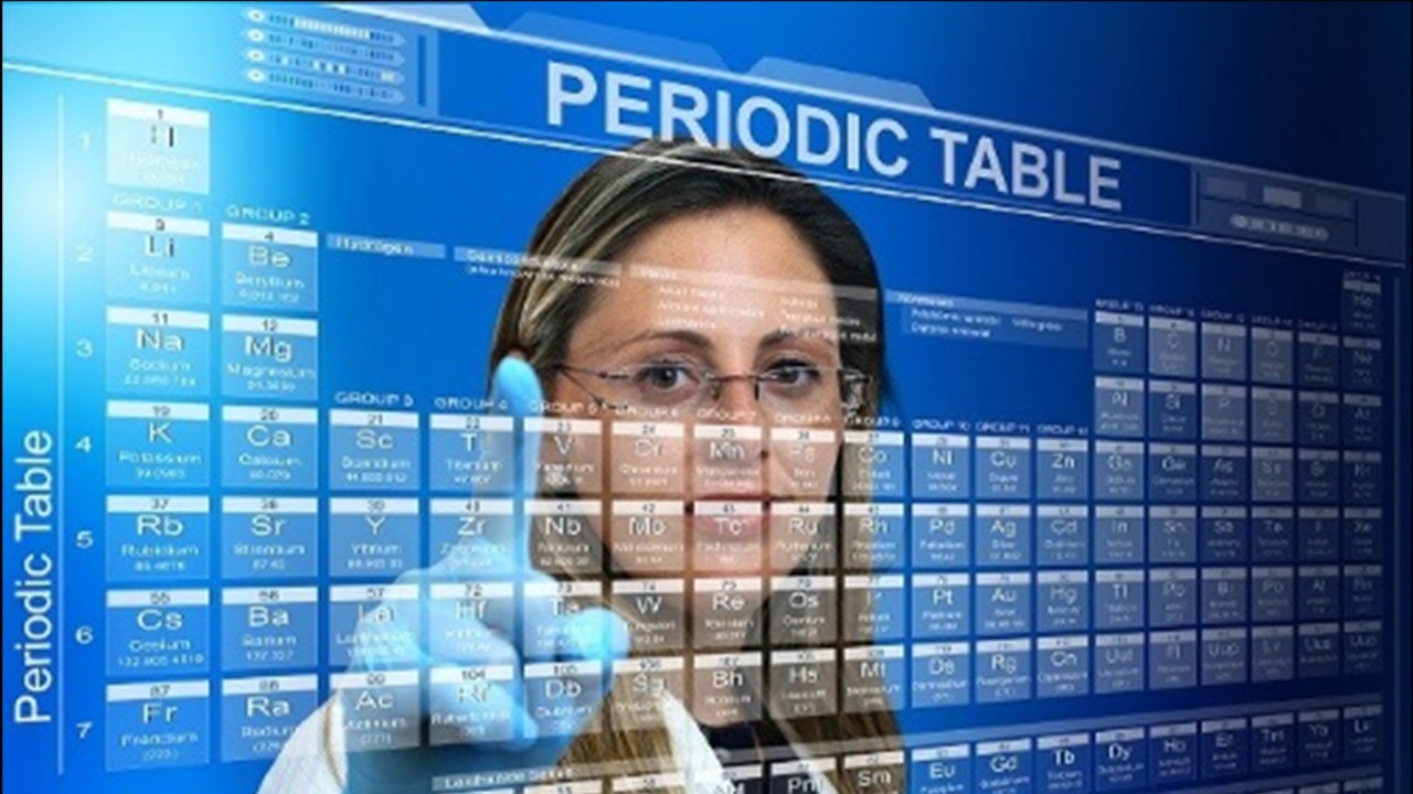 A woman touches a periodic table of the elements.