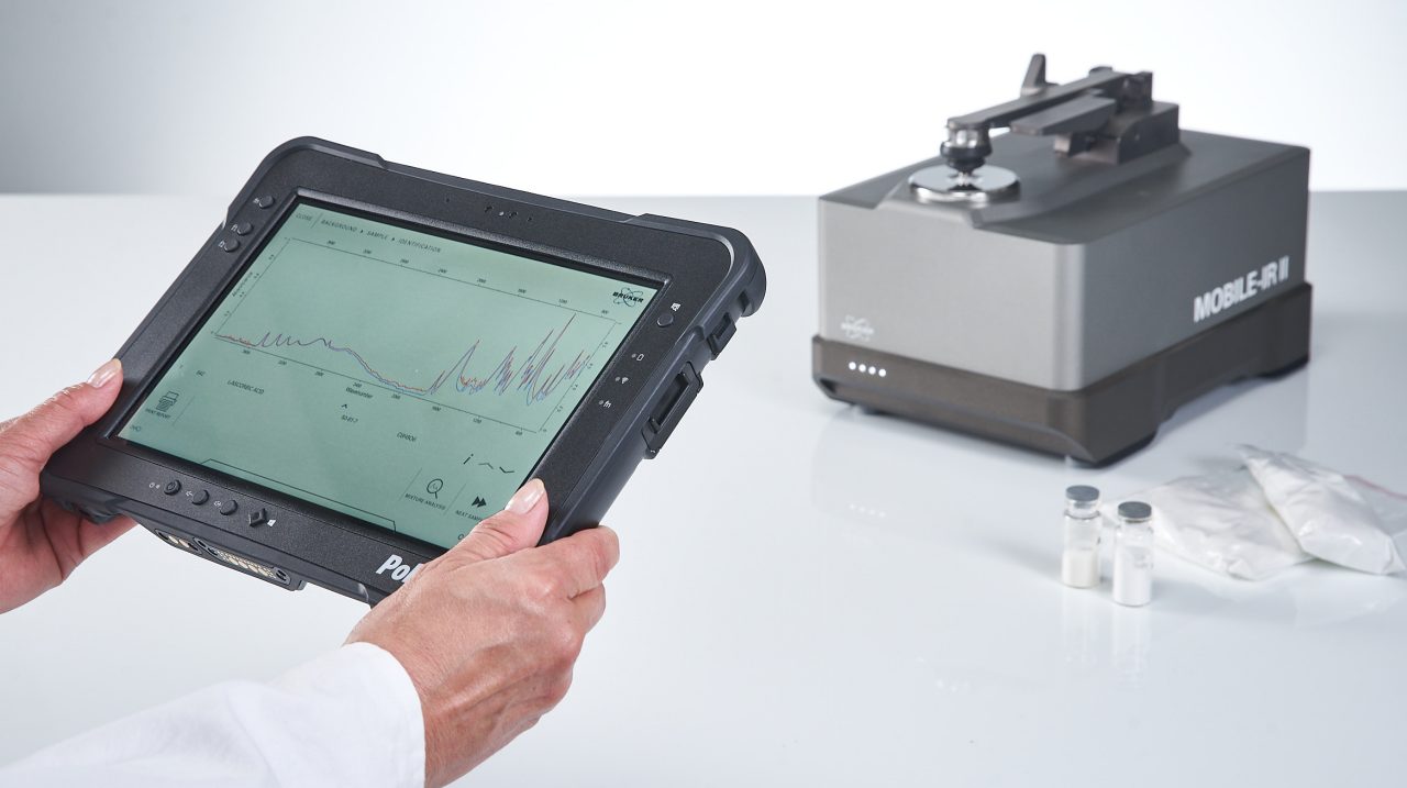 Person holds tablet in hands. Tablet shows a successfull FT-IR measurement. The mobile FT-IR spectrometer is shown out of focus.